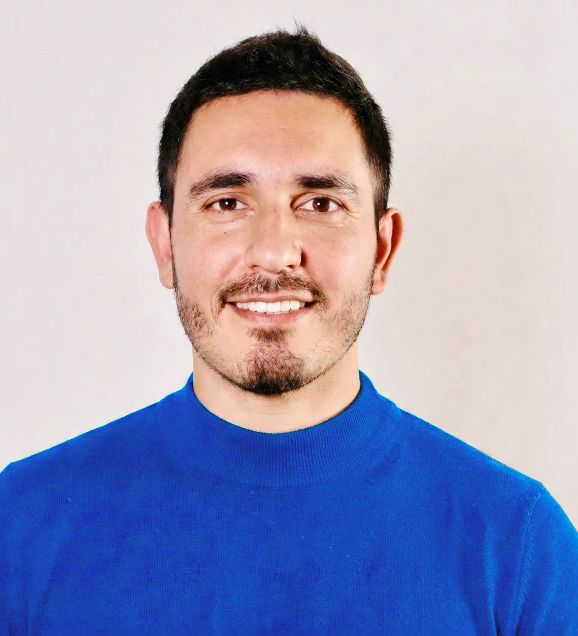 Portrait of Felipe smiling, wearing a bright blue turtleneck sweater